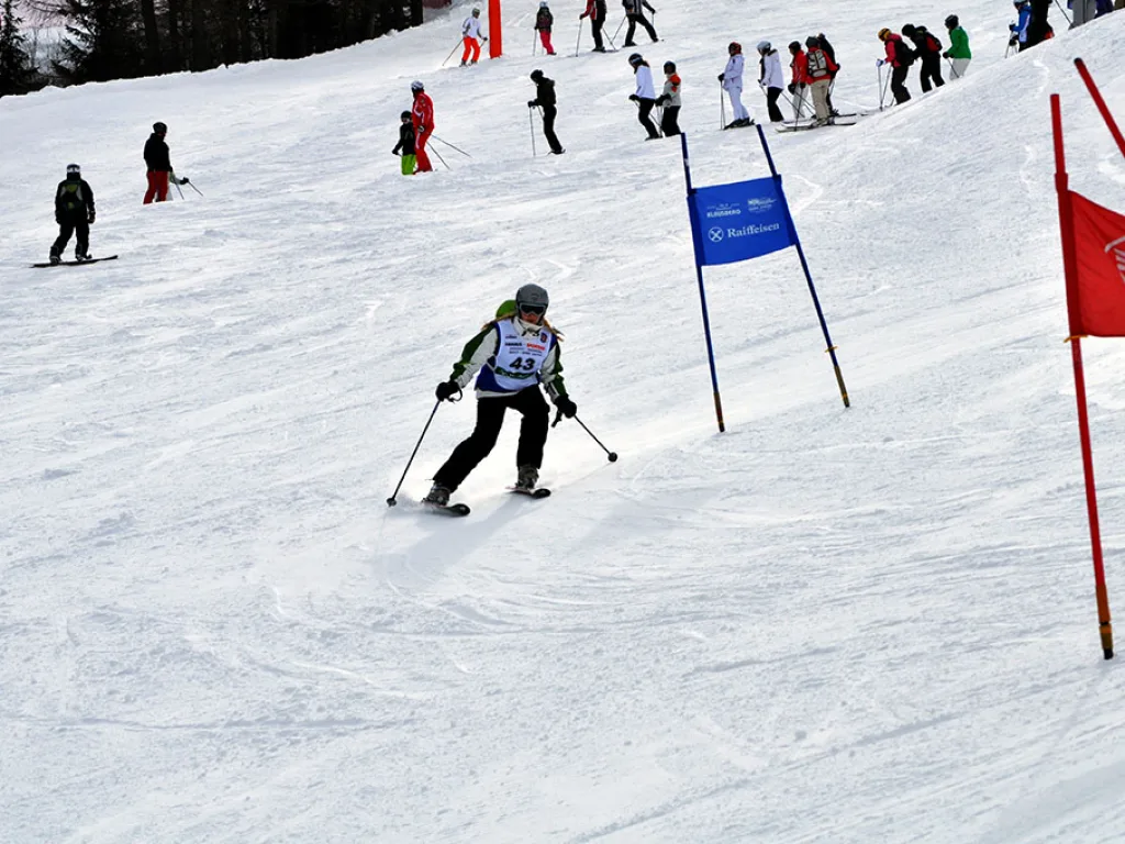 Skifahrerin auf der Strecke, oben stehen Zuschauer am Rand.